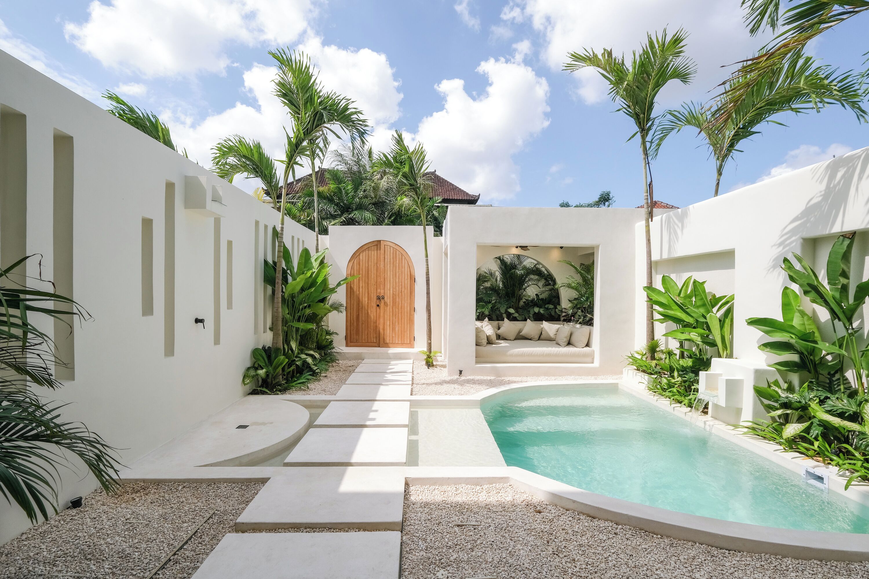 A modern pool area with a wooden door, white walls, and tropical plants.