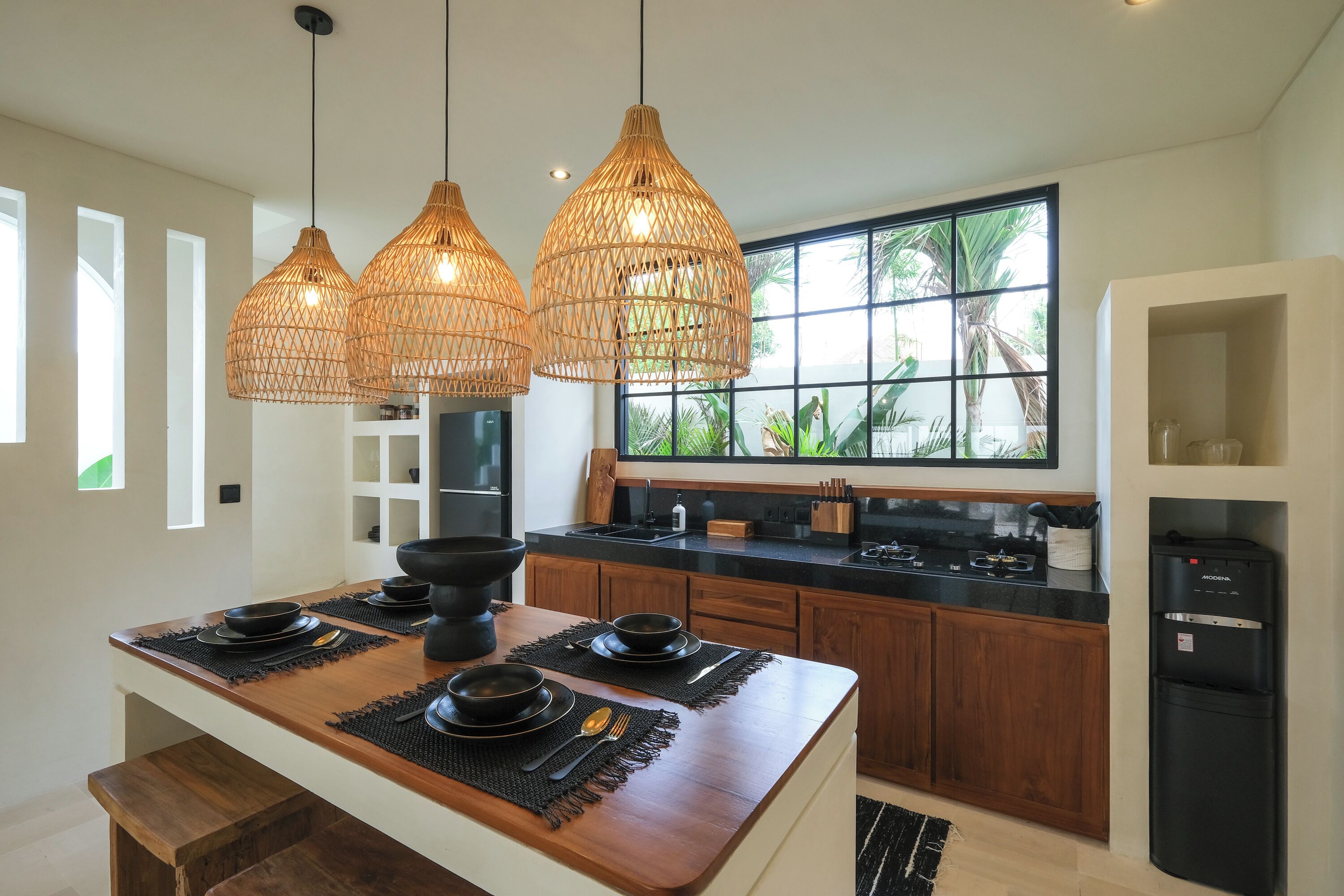 A modern kitchen with a central island, pendant lighting, and a large window with a view of greenery.