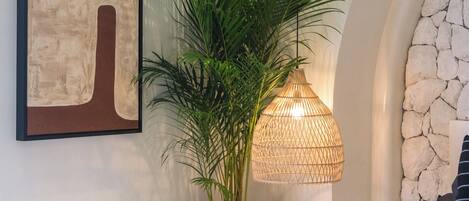 A bedroom with a bed, a potted plant, a hanging light fixture, and a stone wall.