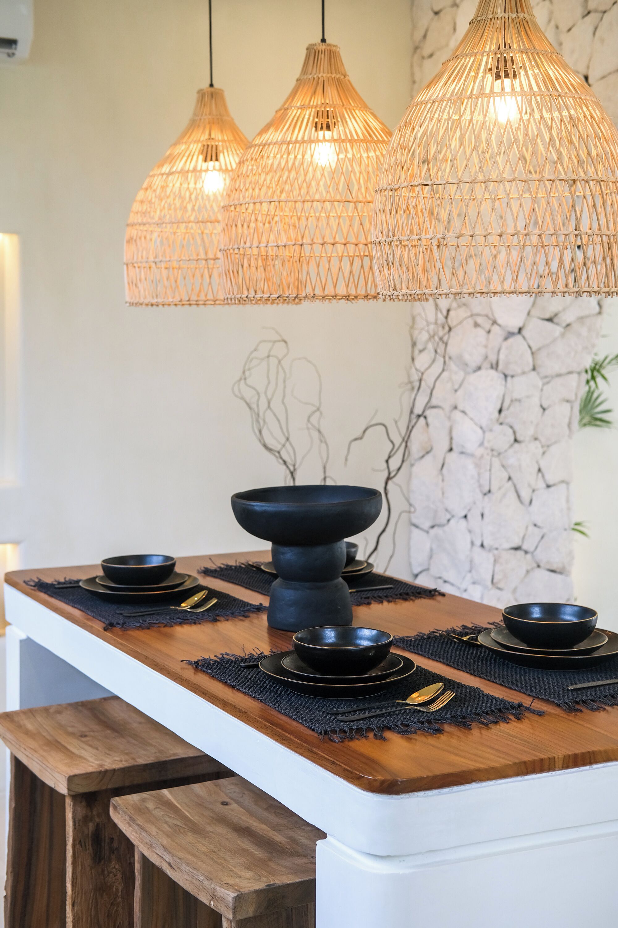 A kitchen with a wooden countertop, black bowls, and a black bowl centerpiece. Three wicker pendant lights hang above.