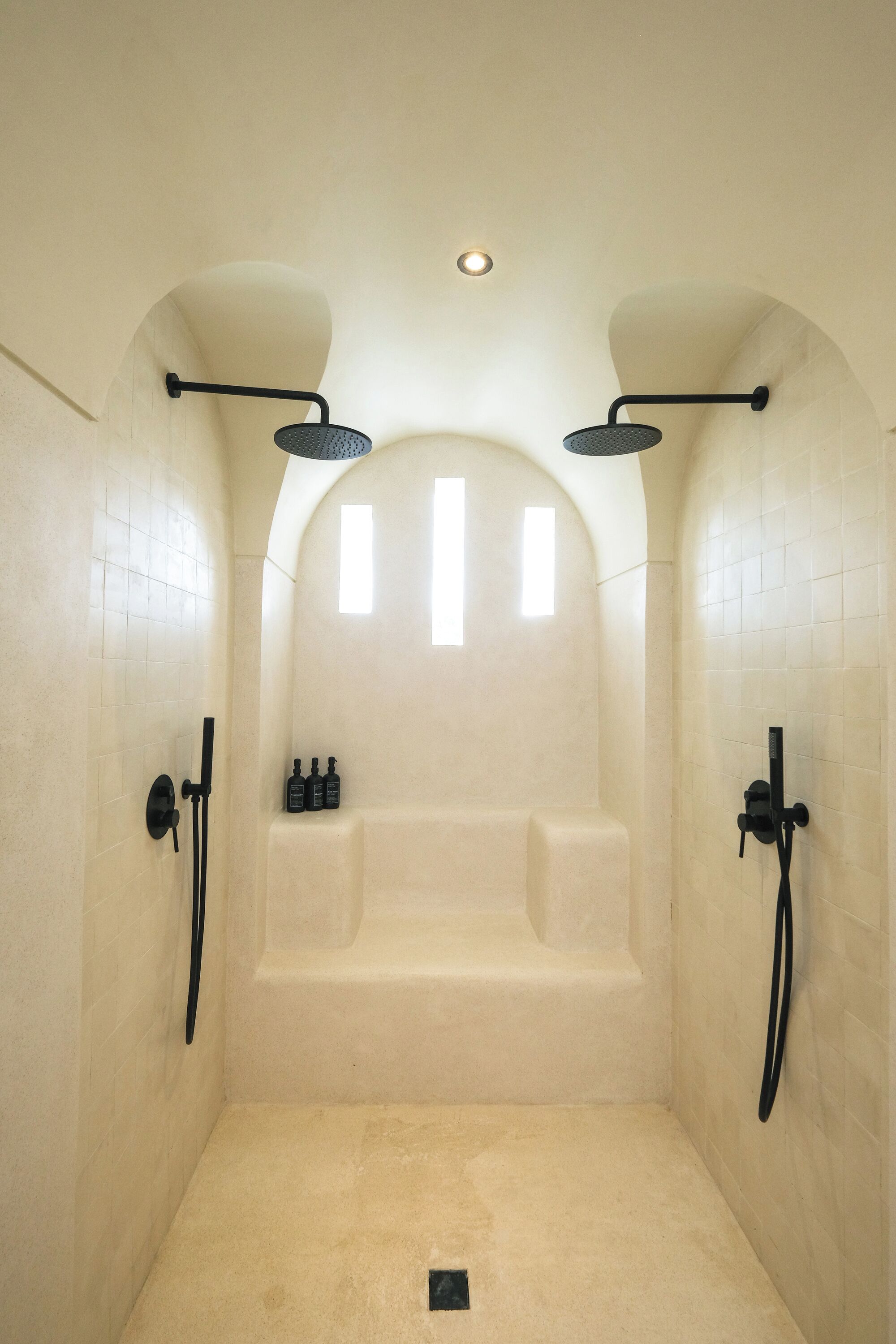 A modern bathroom with a freestanding bathtub, two showerheads, and a small window.