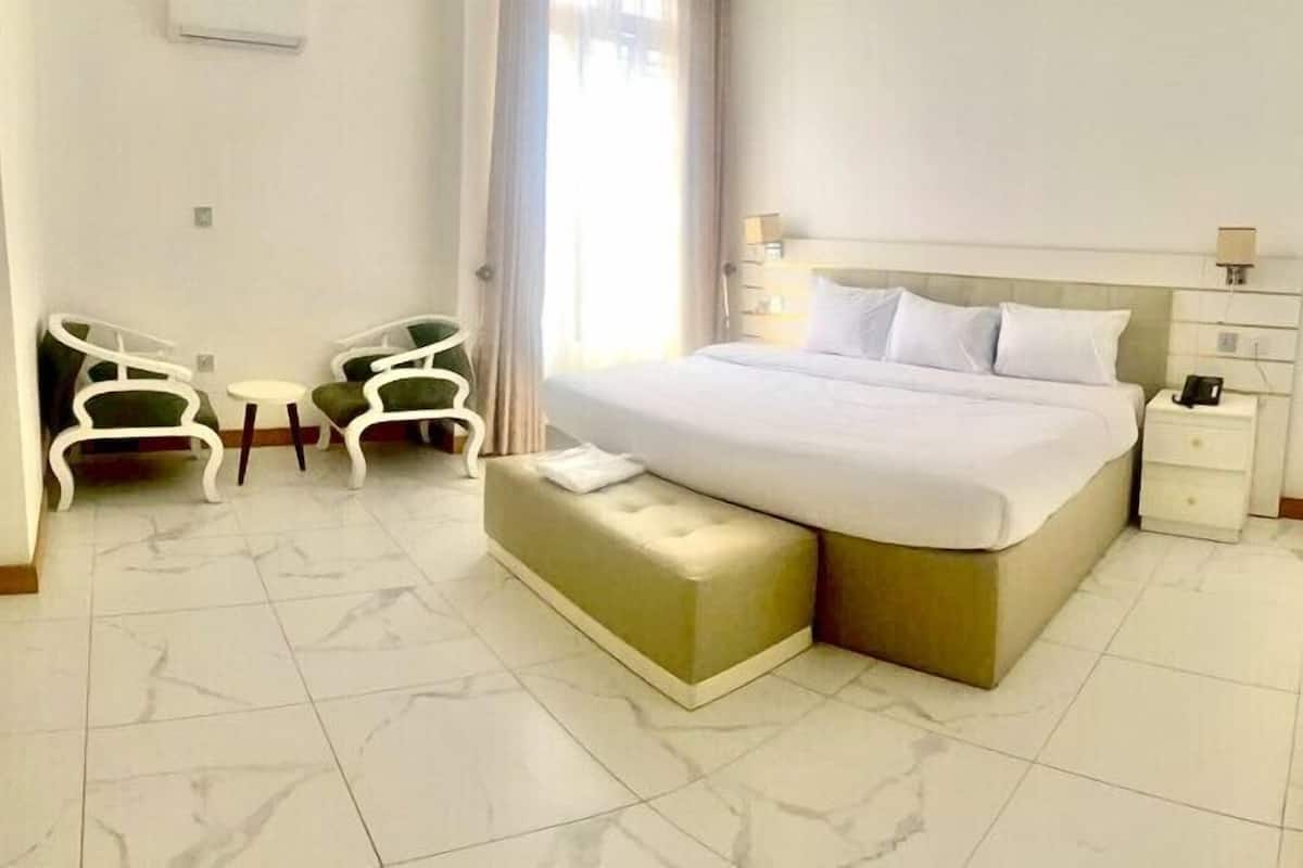 Une chambre d’hôtel avec un lit, deux chaises, une petite table, une table de chevet et une fenêtre avec des rideaux.