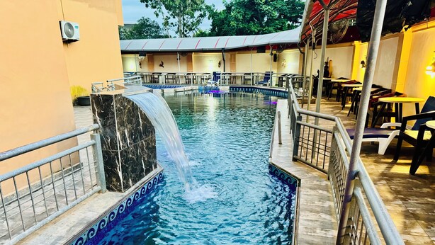 A swimming pool with a marble waterfall feature, surrounded by a tiled deck and metal railings. - Hani Hotels and Suites (Benin City)