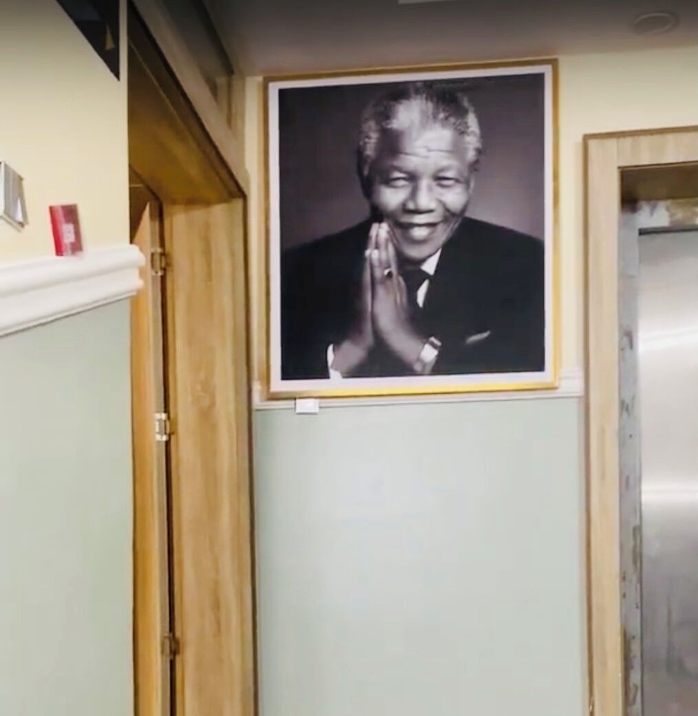 A framed photograph of a person in a suit with their hands pressed together in a gesture of respect or prayer, mounted on a wall above a wooden door.