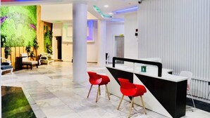 A modern reception area with a reception desk, red chairs, and a green wall with plants. - Hani Hotels and Suites (Benin City)