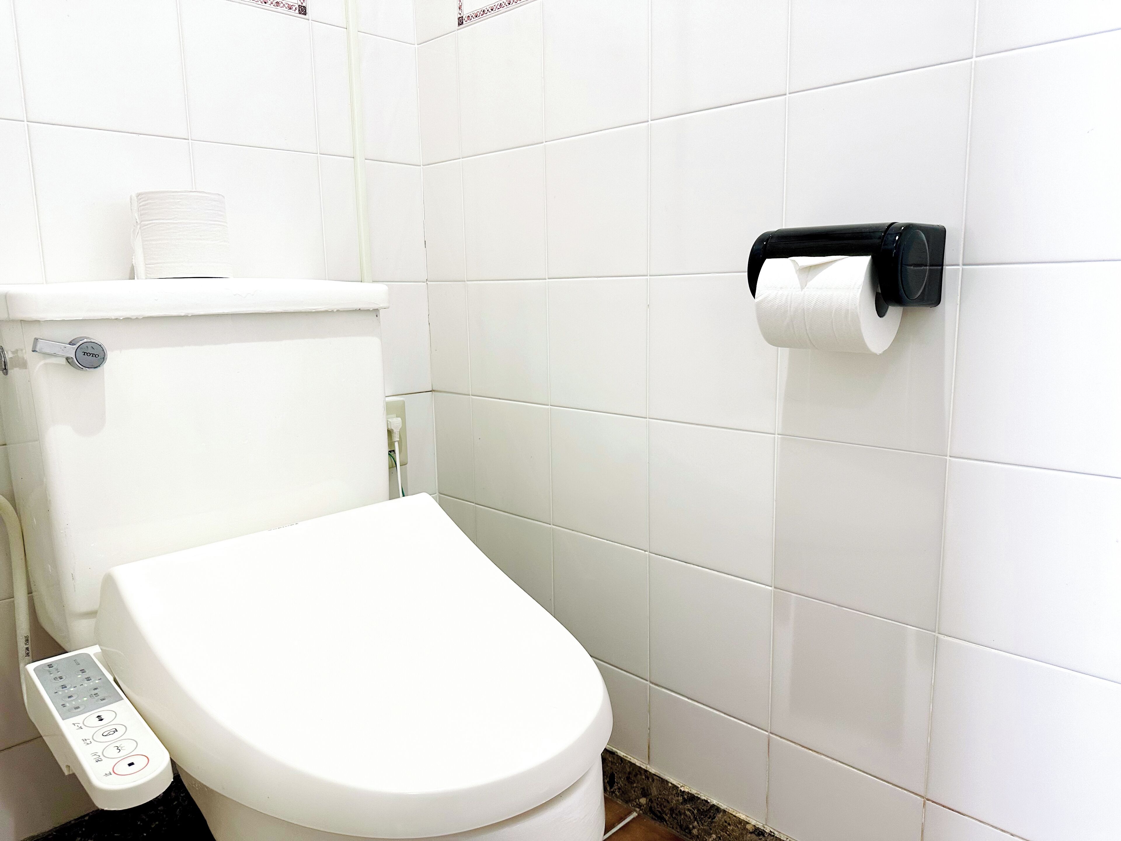 Un inodoro moderno con un panel de control, un dispensador de papel higiénico y un rollo de papel visible.
