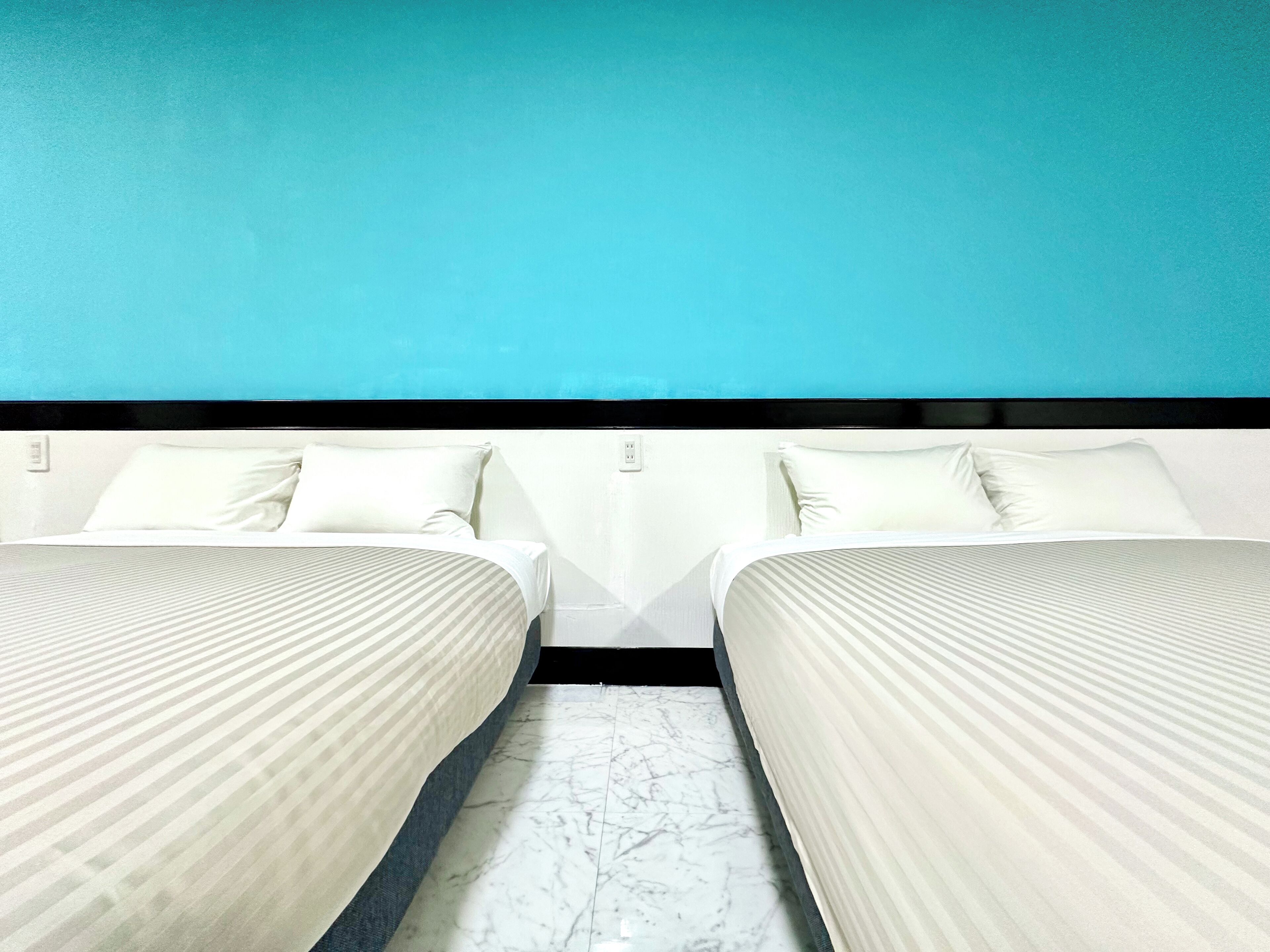 Habitación de hotel con dos camas, piso de mármol y pared color turquesa.