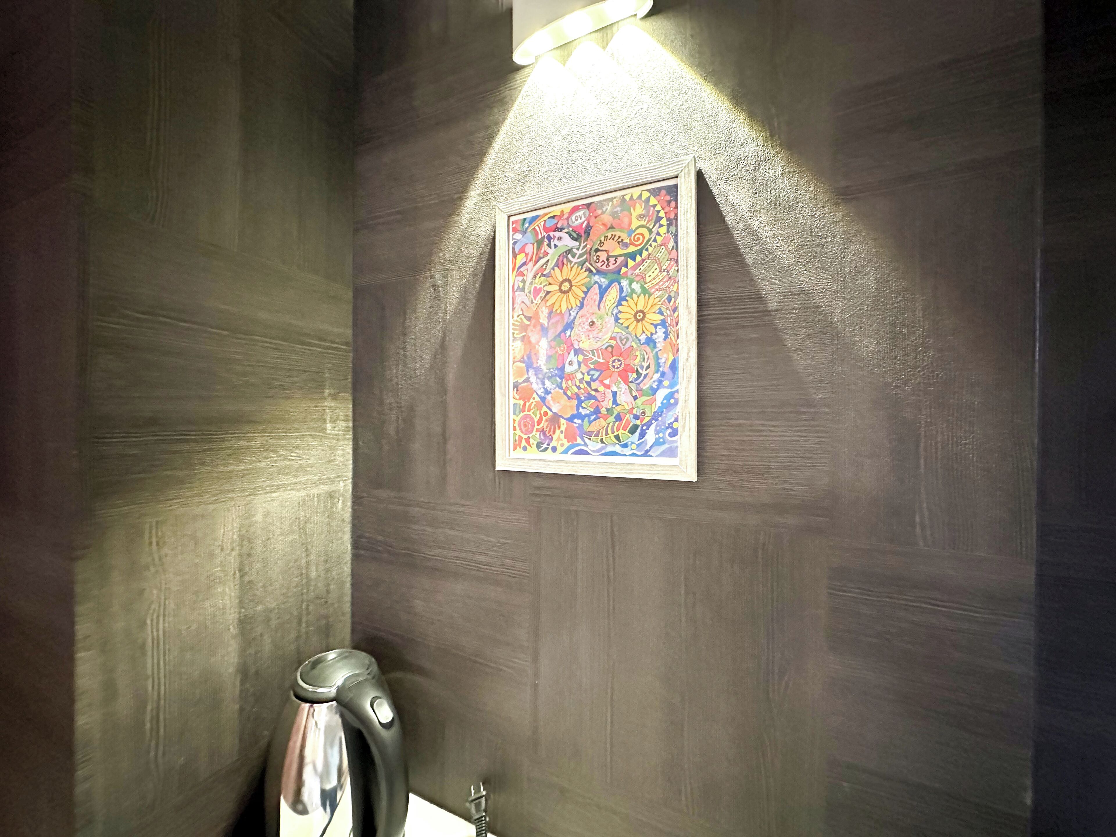 A bathroom with a dark wood wall, a colorful artwork, and a kettle.