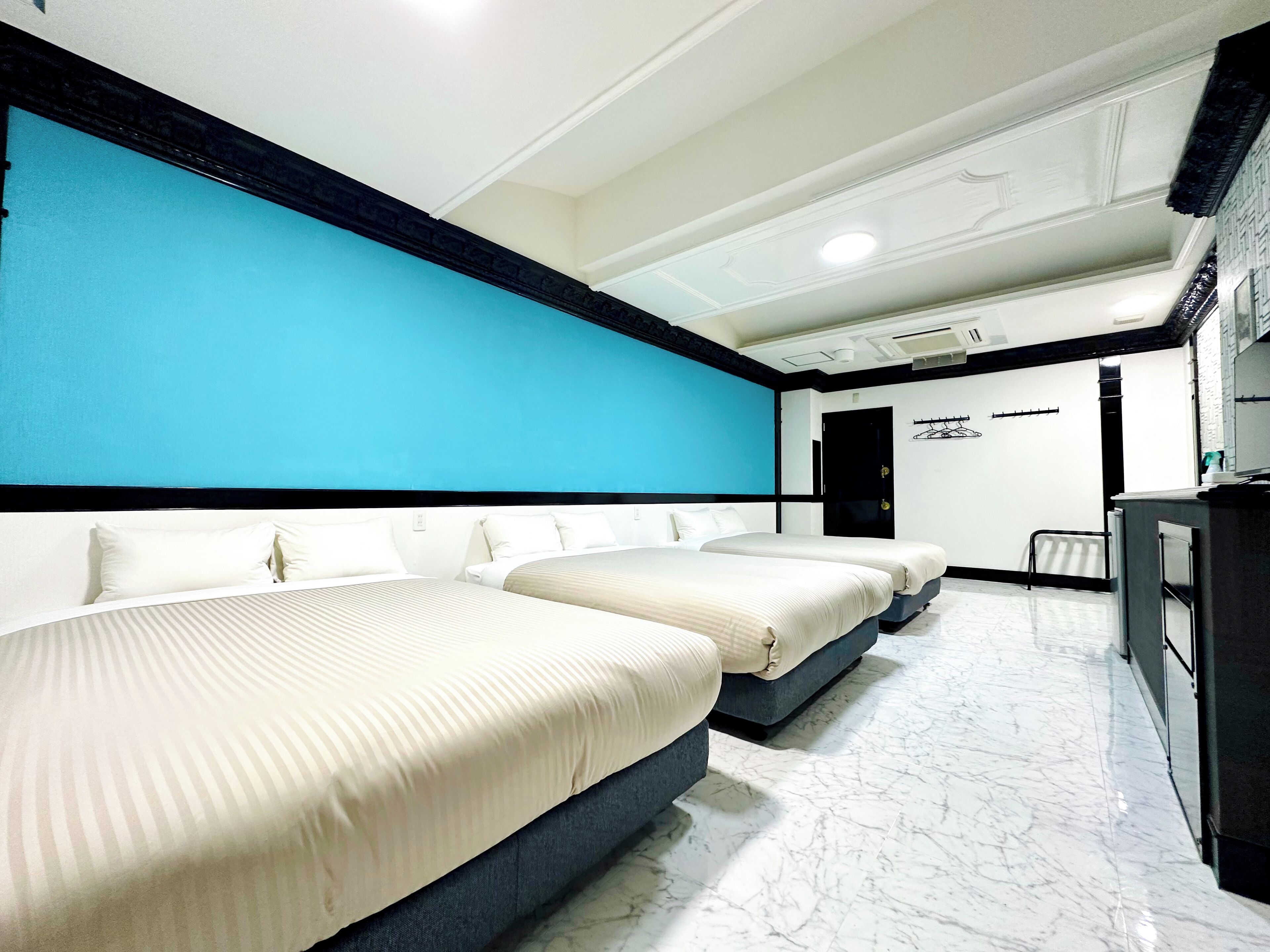 A hotel room with three beds, a blue accent wall, a marble floor, and a desk with a chair.