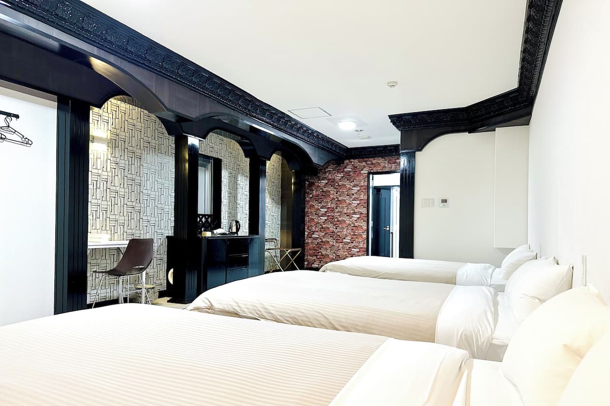 A hotel room with two beds, a desk with a chair, a mirror, and a wardrobe.