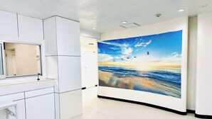 A modern bathroom with a large mirror, white cabinetry, and a wall mural of a beach scene. - ONE STYLE (Naha)