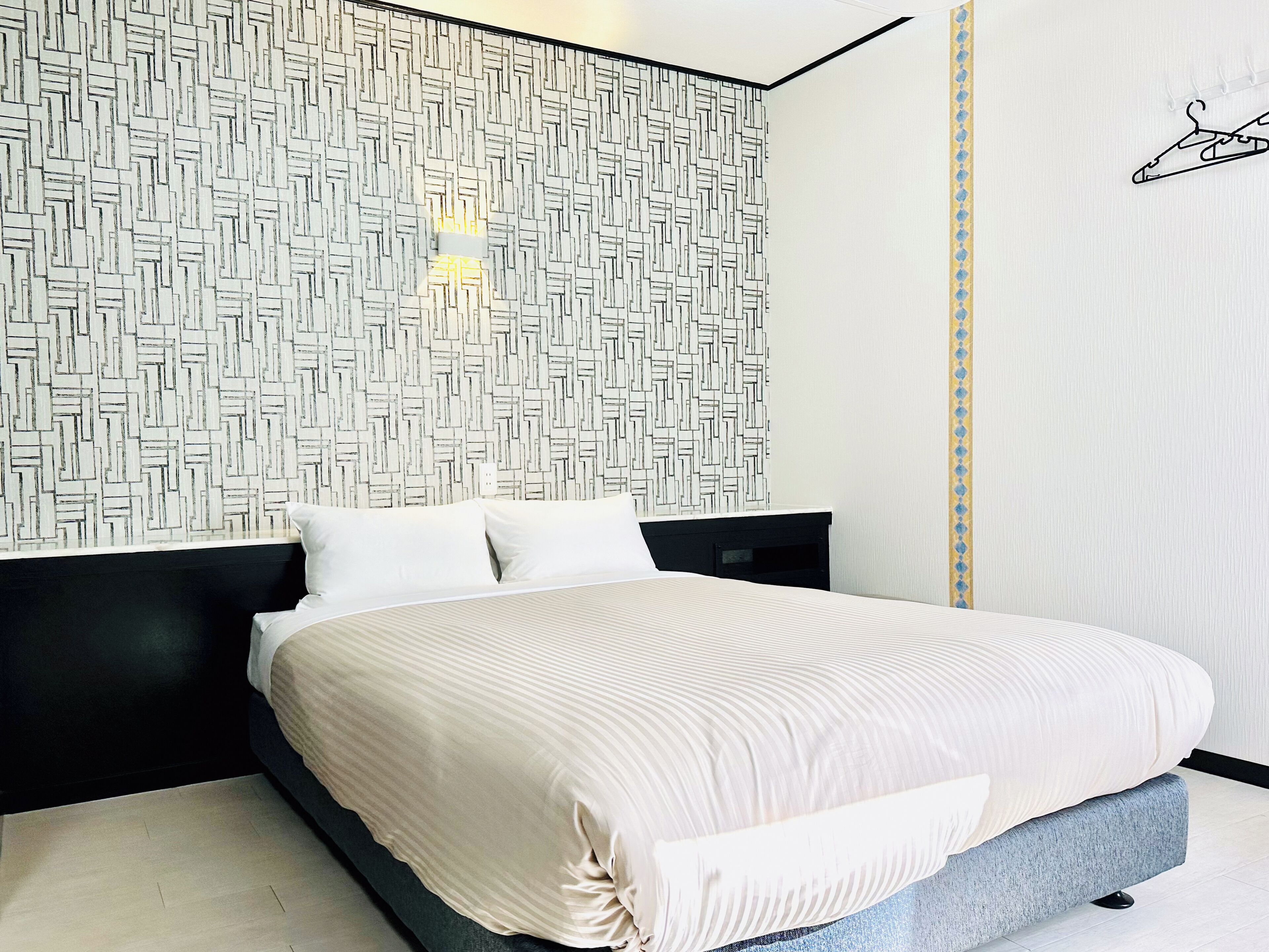 A modern bedroom with a geometric-patterned headboard, a bed with a striped bedspread, and a black nightstand.