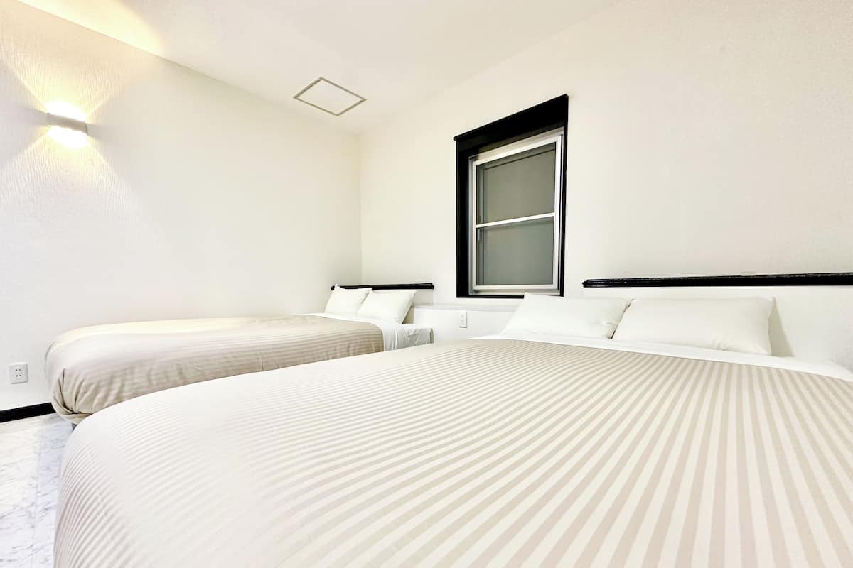 A hotel room with two beds, a window, and a wall-mounted light fixture.