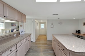 Une cuisine avec des meubles de couleur bois clair, des plans de travail en granit et un plancher en bois.