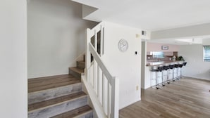 A staircase with wooden steps and white railings leading to a kitchen area with a clock on the wall. - Two Story Private Pool Home Near Bradenton Beach Bayside Paradise (Bradenton)