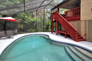 Une piscine avec un escalier rouge et un espace salon abrité.