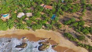 An aerial view of a coastal property with multiple buildings, a beach, and a rocky shoreline.