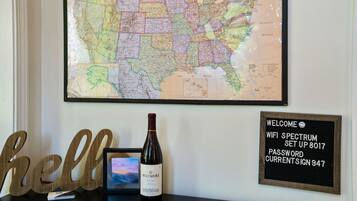 A wall with a large map, a framed welcome sign, a bottle of wine, and a 'hello' sign.