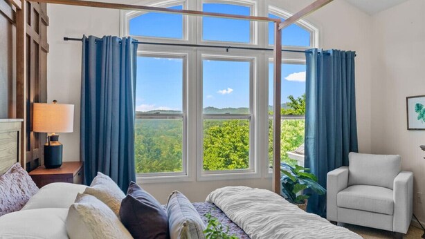 A bedroom with a large window, a bed, a chair, and a nightstand with a lamp. - Theatre~2 Hottubs~MTN Views~Hidden SpeakEasy (Swannanoa)