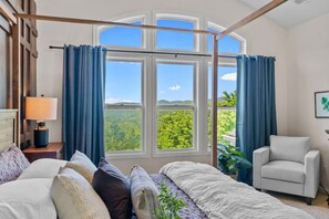 A bedroom with a large window, a bed, a chair, and a nightstand with a lamp. - Theatre~2 Hottubs~MTN Views~Hidden SpeakEasy (Swannanoa)