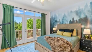 A bedroom with a large bed, a ceiling fan, a nightstand with lamps, and a view of a deck through a sliding glass door. - Theatre~2 Hottubs~MTN Views~Hidden SpeakEasy (Swannanoa)