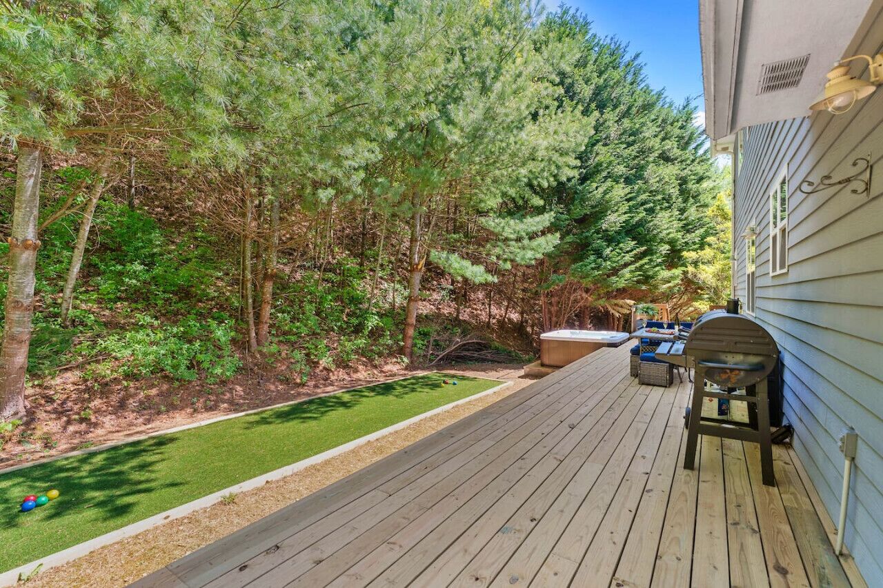 Una terraza de madera con una parrilla, un jacuzzi y una pequeña mesa.