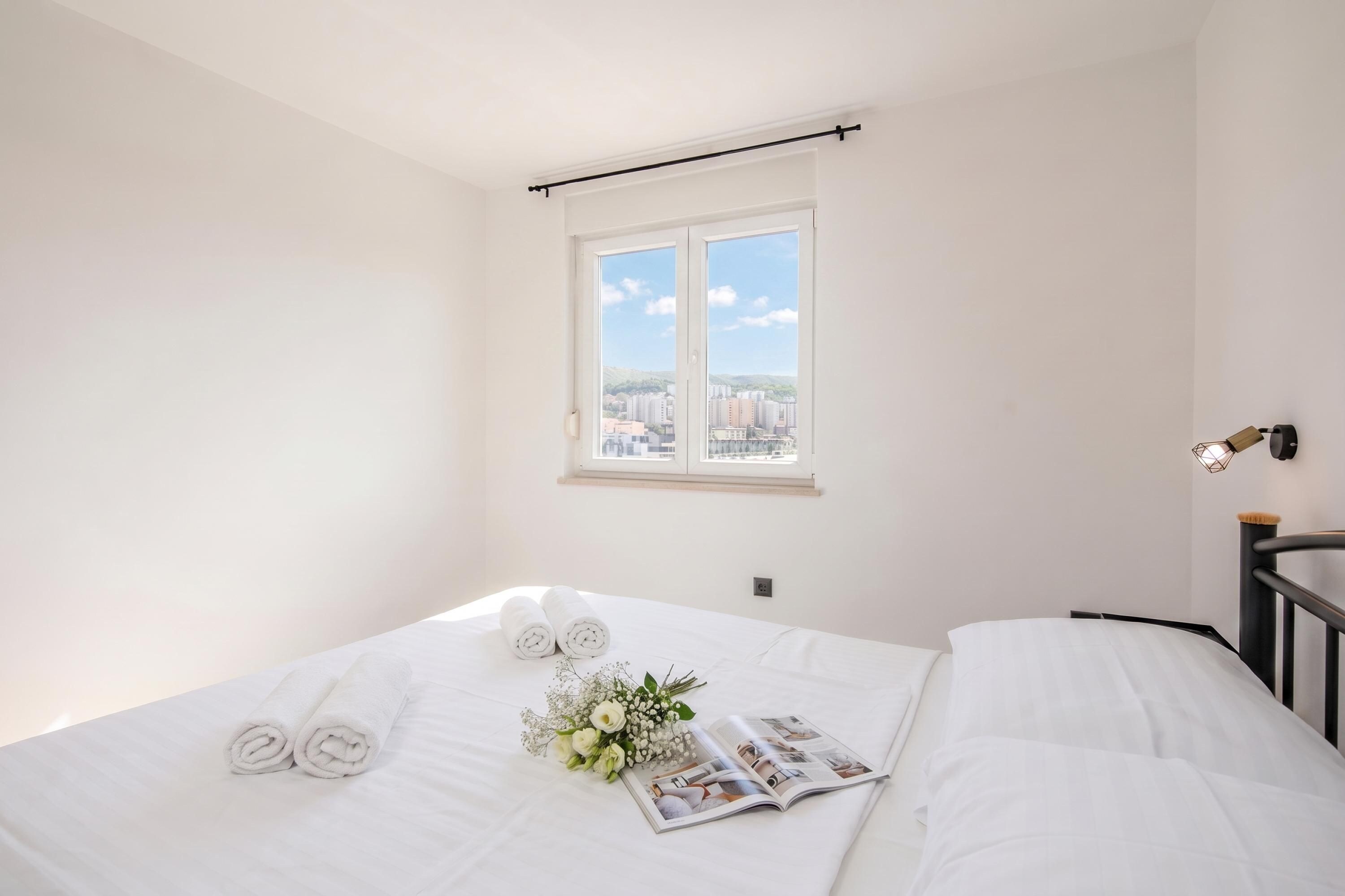 A hotel room with a bed, a window with a city view, and a magazine on the bed.