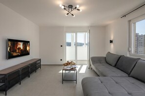 Ein modernes Wohnzimmer mit Flachbildfernseher, Sofa, Couchtisch und Deckenleuchte.