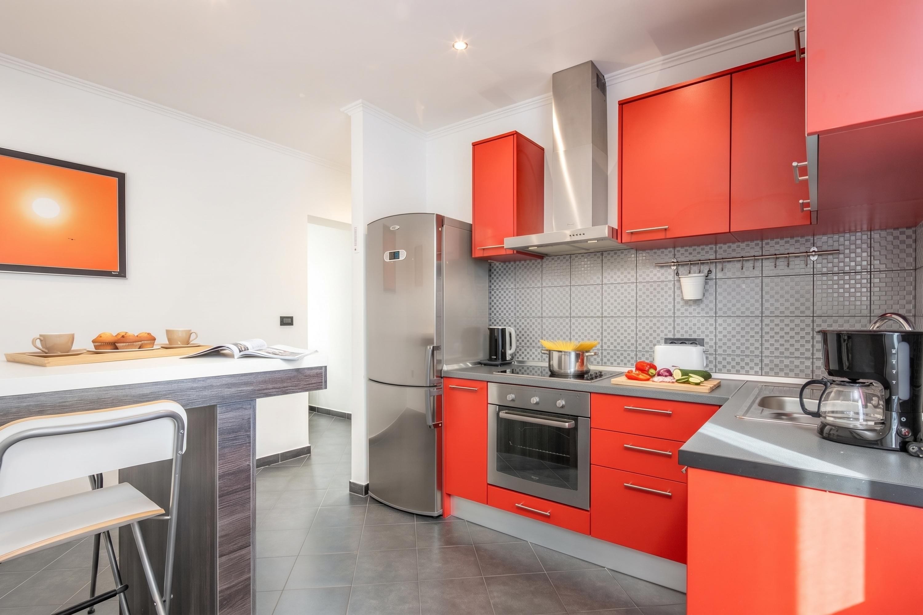 A modern kitchen with red cabinets, stainless steel appliances, and a tiled backsplash.