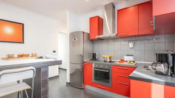 A modern kitchen with red cabinets, stainless steel appliances, and a tiled backsplash.