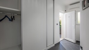 Un couloir avec une porte coulissante, un porte-manteau avec des cintres et une porte donnant sur une autre pièce.