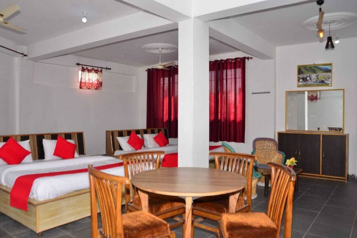 A hotel room with two beds, a dining table, and chairs. There is a mirror and a cabinet in the room.