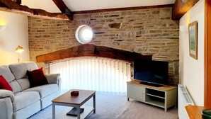 Ein Wohnzimmer mit Steinwand, einer Couch, einem Couchtisch, einem Fernseher und einem Fenster mit Jalousien.