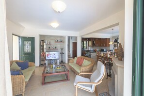 A spacious living area with a sofa, armchair, and coffee table, connected to a kitchen with wooden cabinets and a dining area.
