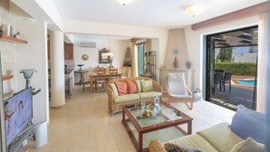 Amplia sala de estar con sofá, mesa de centro y comedor. Cuenta con televisor, chimenea y vistas al exterior.