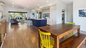 A modern kitchen with a central island, a dining area with a wooden table and yellow chairs, and a view through large glass doors.