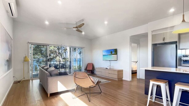 A modern living room with a sofa, a dining area with stools, a TV, and a kitchen area with a fridge. - Pet-Friendly 3-Bed Coastal Gem Near Long Beach (Long Beach)