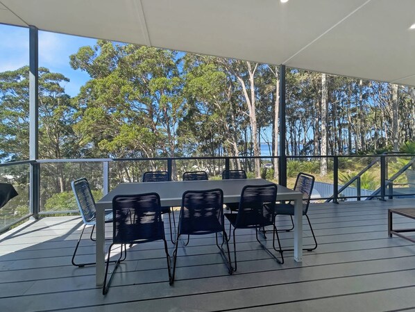 Un espacio al aire libre techado con una mesa y sillas, ventanas amplias y vistas a árboles y una masa de agua.