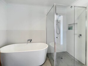 Un baño moderno con una bañera independiente, ducha con mampara de vidrio y pared de azulejos blancos.