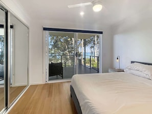 A bedroom with a bed, a nightstand, a lamp, and a balcony with a view of trees and the sea. - Pet-Friendly 3-Bed Coastal Gem Near Long Beach (Long Beach)