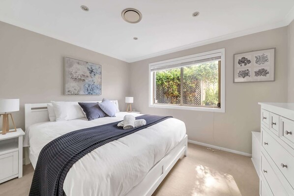 A bedroom with a bed, bedside tables, a window with a view, and artwork on the walls.