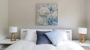 A bedroom with a bed, two bedside tables, and a wall-mounted abstract painting. - 3-Bed with Beach Views and Entertainment Area (Denhams Beach)
