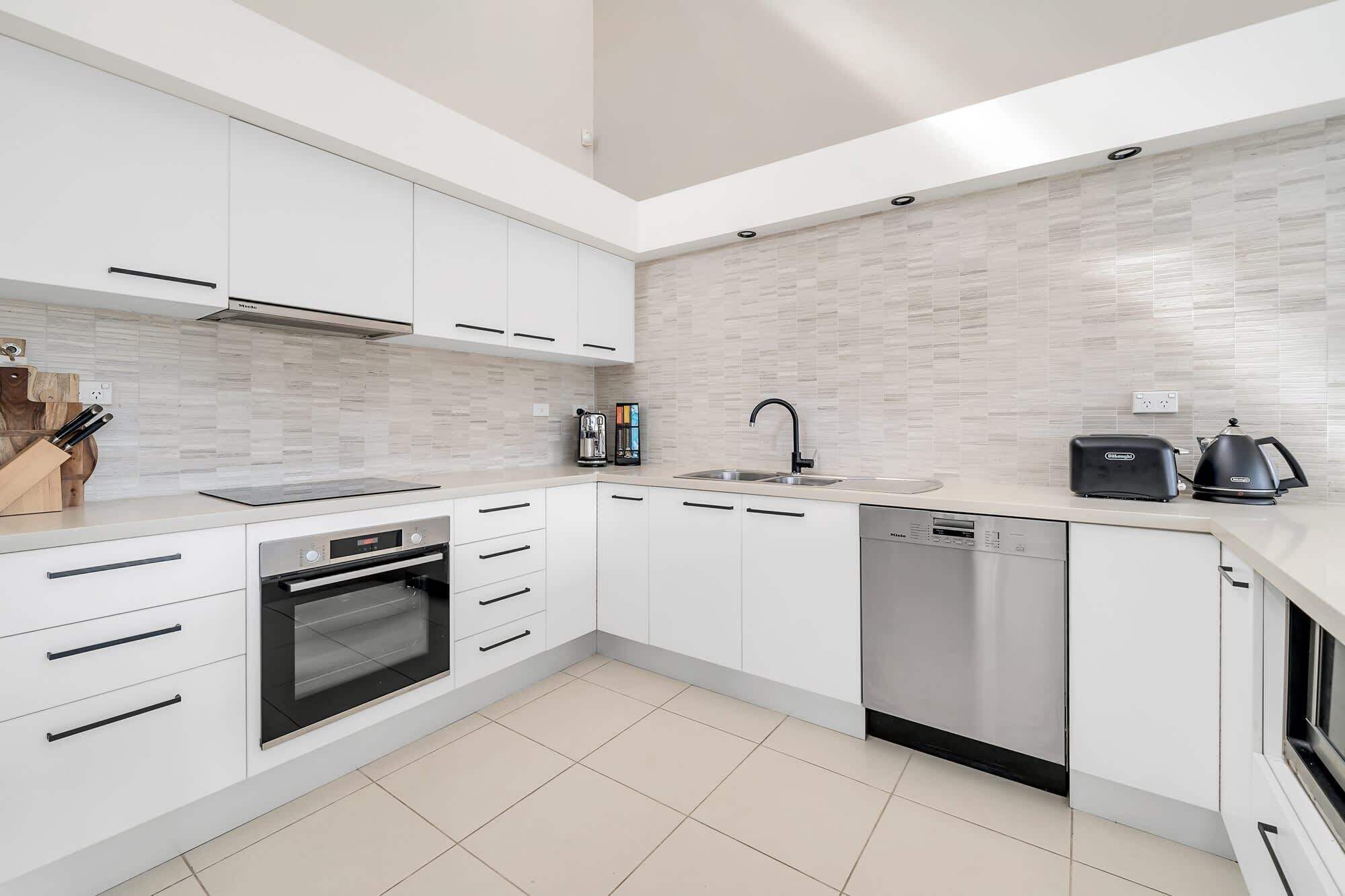 A modern kitchen with white cabinetry, a built-in oven, a dishwasher, and a coffee maker.
