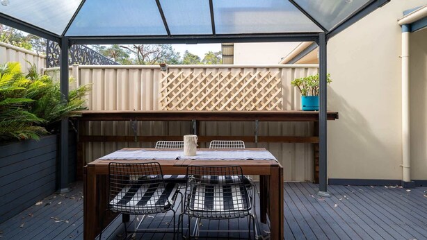 A covered patio with a table and chairs, a wooden fence, and potted plants. - 3-Bed with Beach Views and Entertainment Area (Denhams Beach)