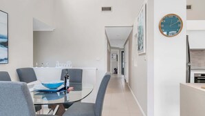 A modern dining area with a glass table, grey chairs, and a clock on the wall. - 3-Bed with Beach Views and Entertainment Area (Denhams Beach)