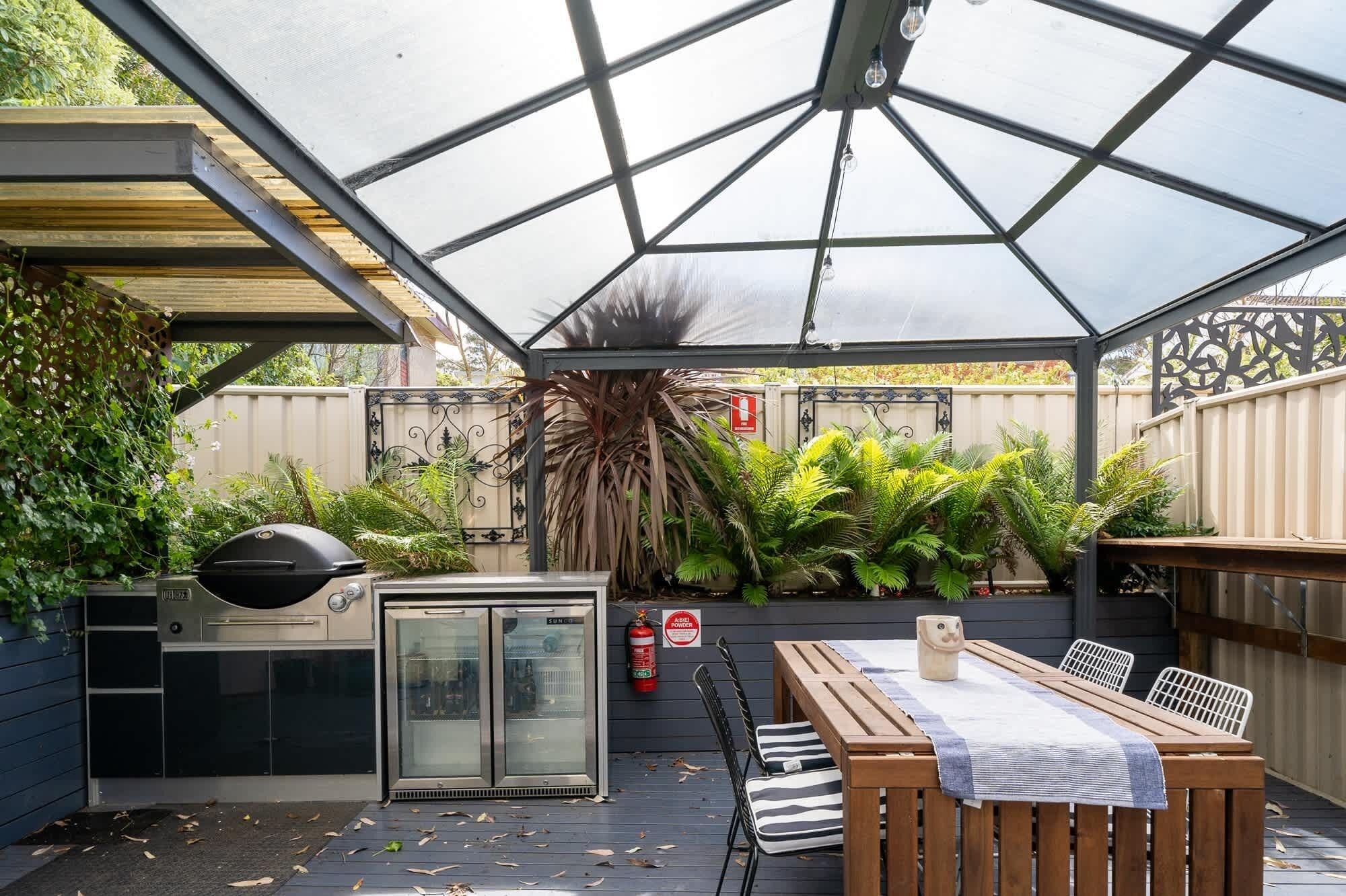 A covered outdoor area with a grill, refrigerator, and seating.