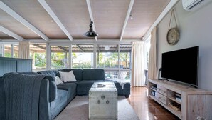 A living room with a sectional sofa, a television, and a wooden entertainment unit. - Secluded 3-Bed Retreat Moments to the Beach (Surf Beach)