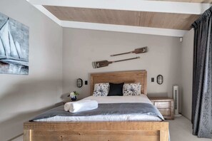A bedroom with a wooden bed, a wall-mounted wooden paddle, a bedside table with a lamp, and a large window with curtains.