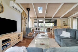 Un soggiorno con una grande TV a schermo piatto, arredamento in legno, un camino in pietra e vista panoramica attraverso ampie finestre.