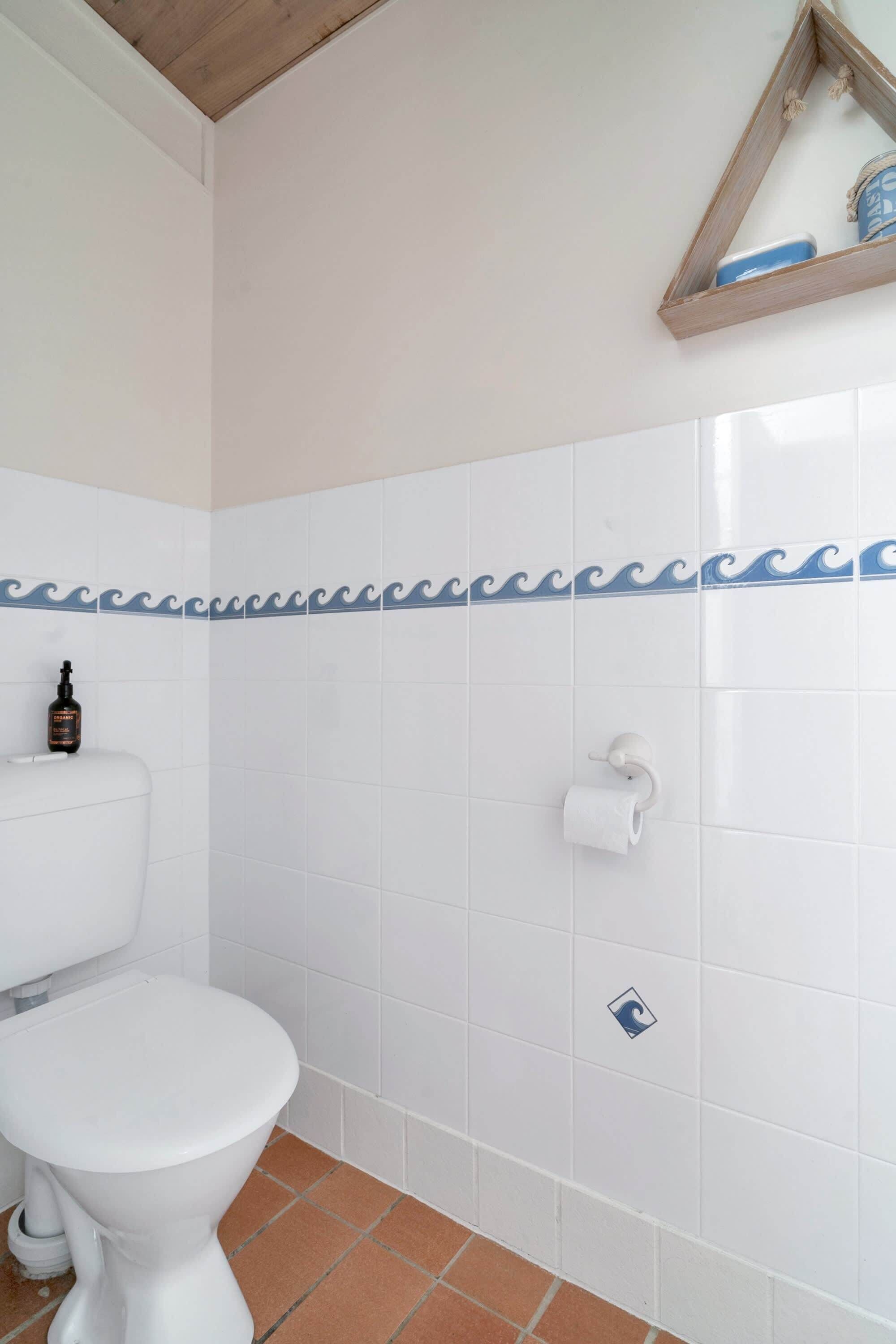 Ein Badezimmer mit Toilette, Ablagefläche für Pflegeprodukte und Fliesen mit Wellenmuster.